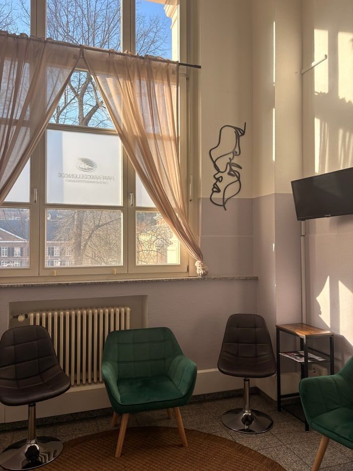 Wartebereich der Praxis: ein grüner Samtsessel vor einem hohen Fenster im Morgenlicht